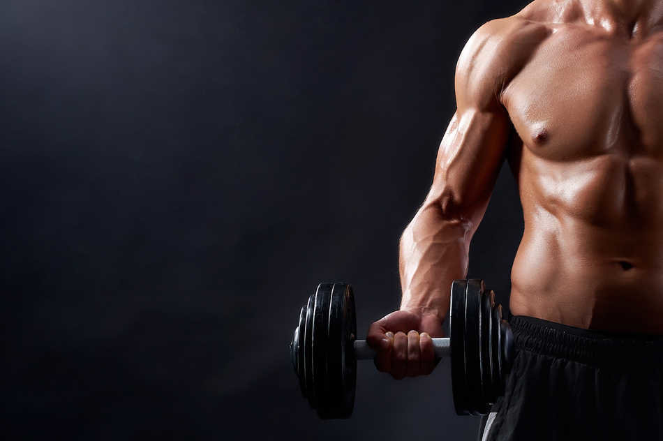 True hard worker. Cropped closeup of a strong muscular male holding a dumbbell posing against black background