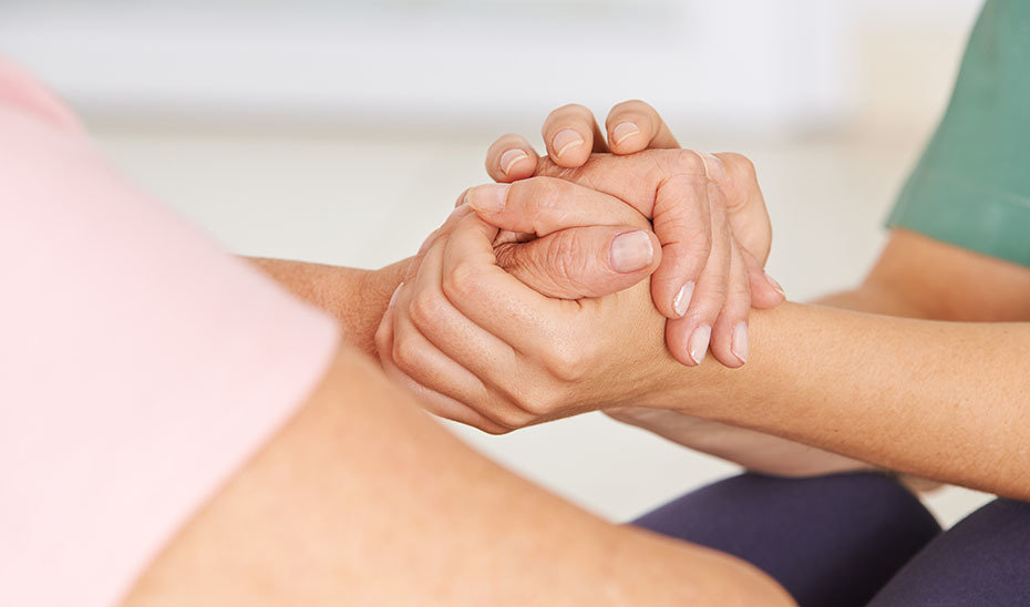 Krankenschwester hält die Hände einer Senorin zum Trost und zur Unterstützung