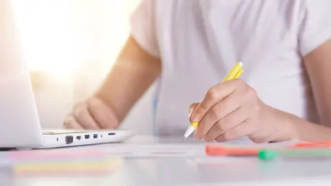 Woman hands with yellow pen writing something on peper, working online, female wearing white casual t shirt working on laptop and using wireless Internet, designer or programmer sitting at table.