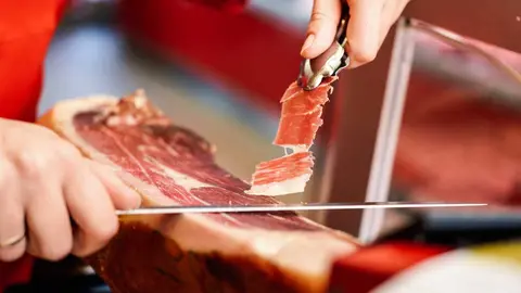 Close-up of professional cutter carving slices from a whole bone-in serrano ham
