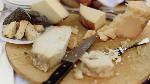Knife and fork lie on wooden plate with different kinds of cheese