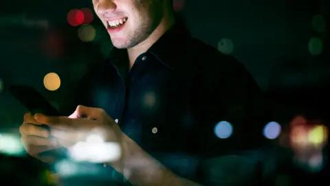 Happy young adult male using a smartphone in a night cityscape