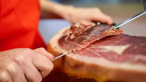 Close-up of professional cutter carving slices from a whole bone-in serrano ham